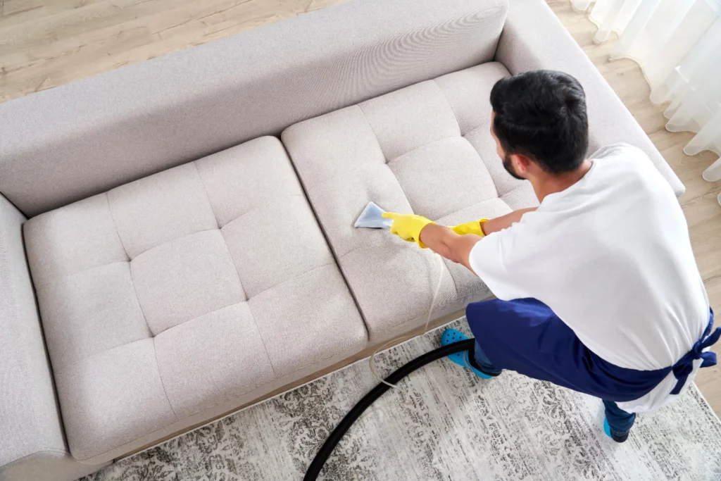 Technicien nettoyant un canapé en tissu clair avec une éponge