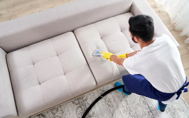 Technicien nettoyant un canapé en tissu clair avec une éponge